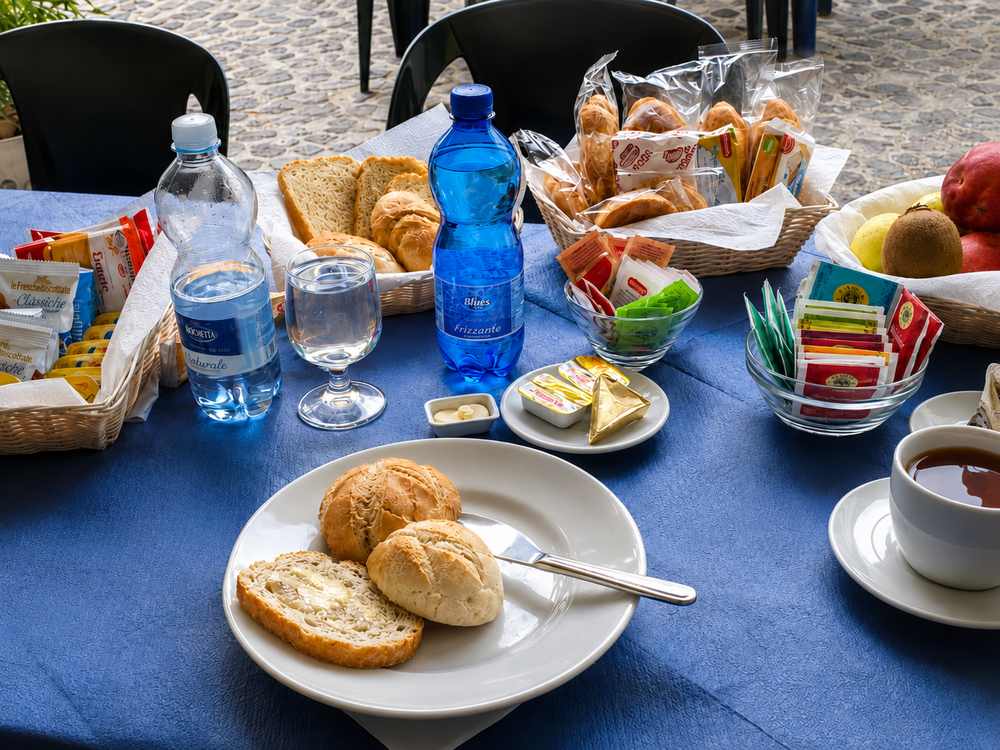 Tavolo della colazione all'aperto con pane, frutta, tè e caffè
