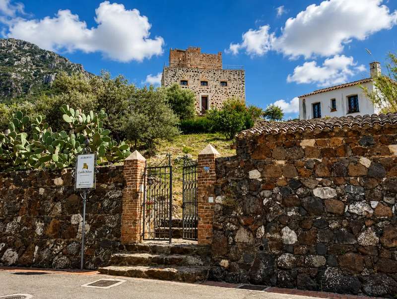 Vicolo di Galtellì con muro di pietra, cancello in ferro e la torre antica sopra