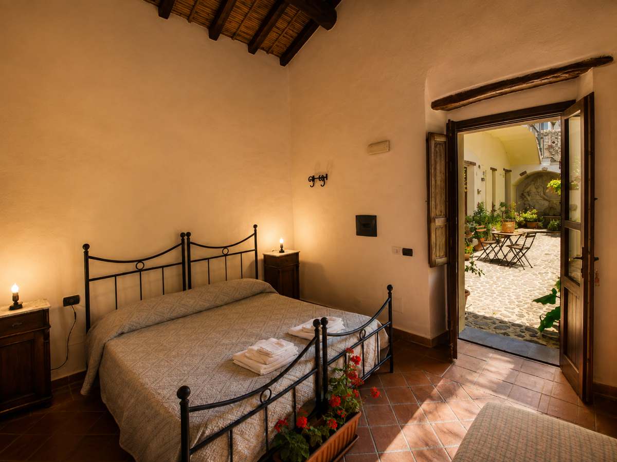 Camera con letto in ferro, coperta tessuta e pavimento in terracotta